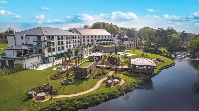 Aerial view of the Culloden Estate and Spa in Holywood, showing the white hotel building, landscaped grounds, riverside gazebos and garden terraces under a blue sky
