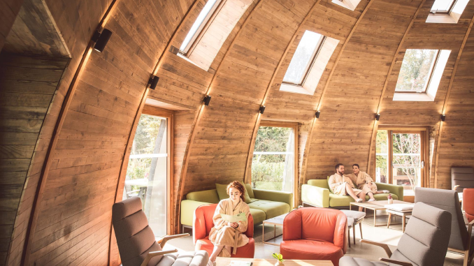Guests in white robes relaxing inside the curved timber spa lounge at Galgorm, County Antrim, with skylights flooding the vaulted wooden interior with natural light