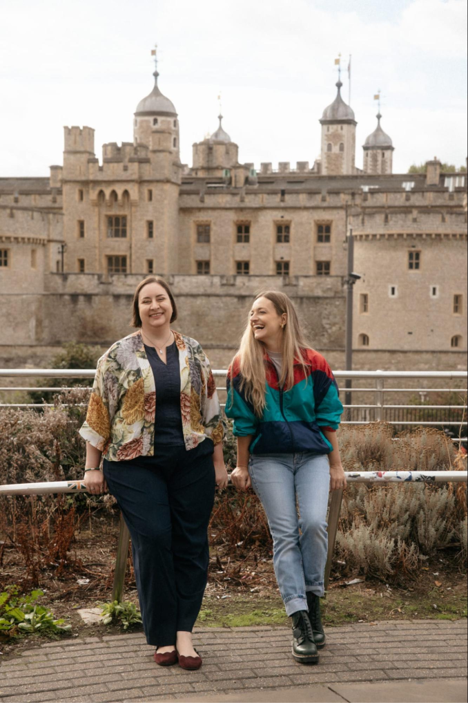 Two Tiernan Travel team members laughing together beside a railing, with the Tower of London in the background
