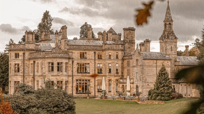 A grand Victorian Gothic country house hotel in sandstone with turrets, a clock tower, and outdoor dining terrace on an overcast autumn day